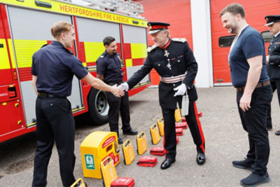 Charity founders and representatives from Hearts for Herts Charity shaking hands with firefighters in front of a fire truck, with donated Mindray BeneHeart C1A AED units displayed